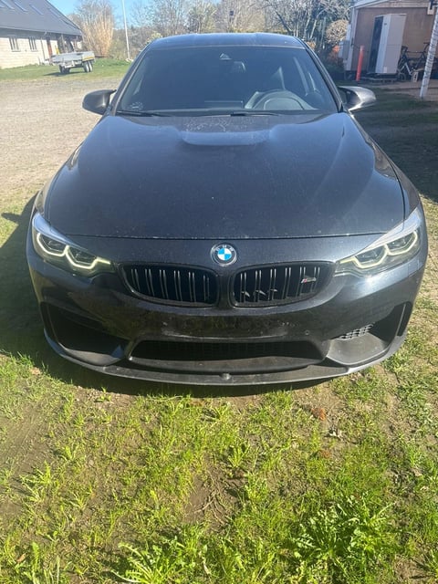 Gray BMW sedan parked on grass driveway facing forward, showing illuminated LED headlights and distinctive grille