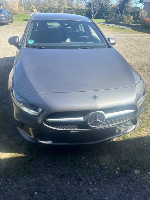 Silver Mercedes-Benz sedan parked in a driveway with trees and residential property in background